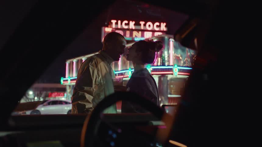 Couple kissing in front of a diner with a neon sign at night