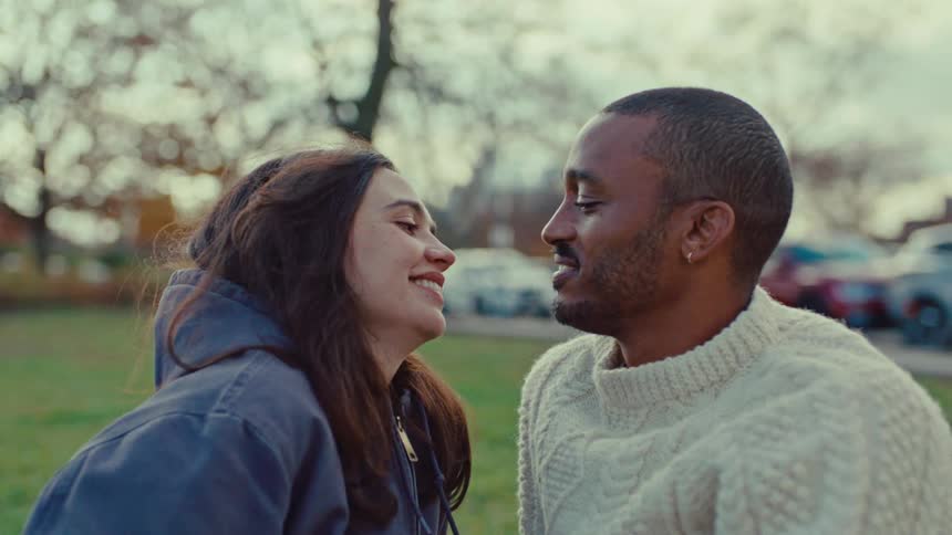 Man and woman close to each other in a park with cars in the background