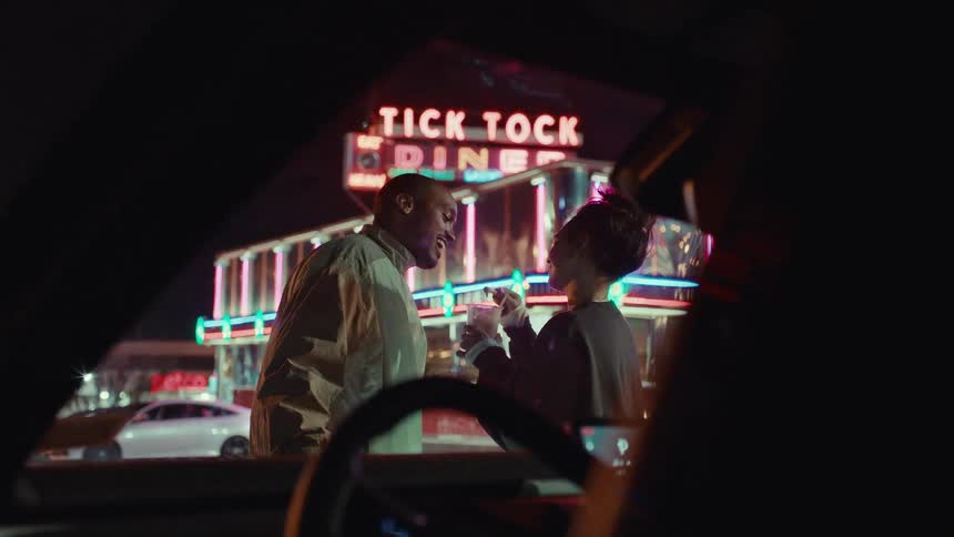 Couple sharing a dessert in front of a diner with a neon sign at night