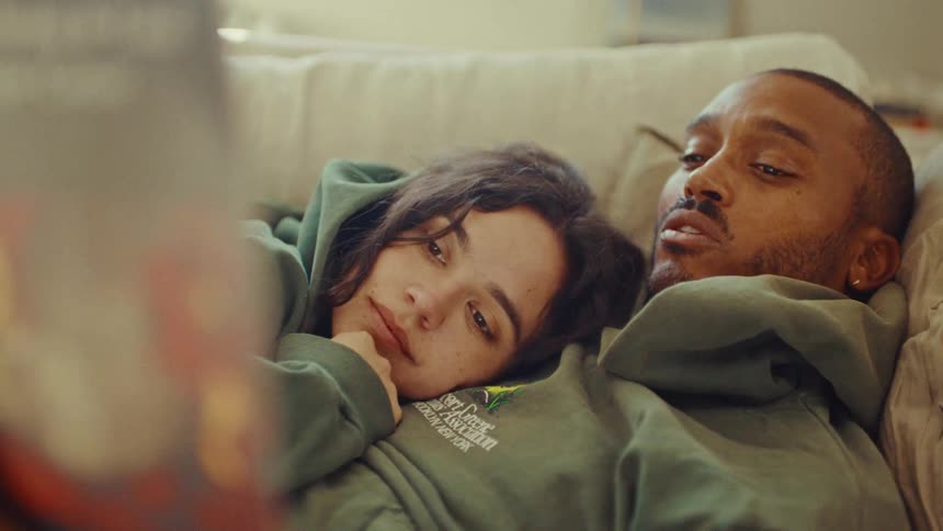 Woman listens while lying on a man as he reads in the living room during the daytime