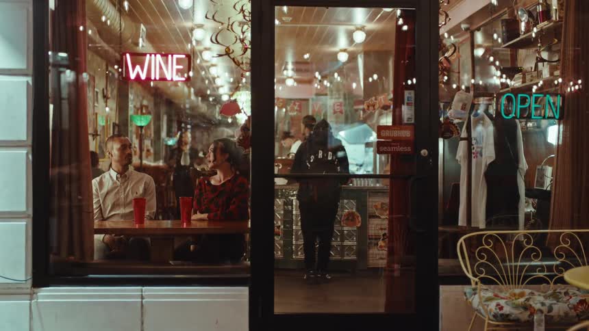 Couple sitting at a table inside a restaurant with wine and open neon signs