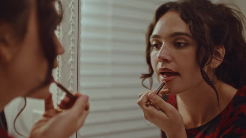 A woman putting on lipstick in a mirror