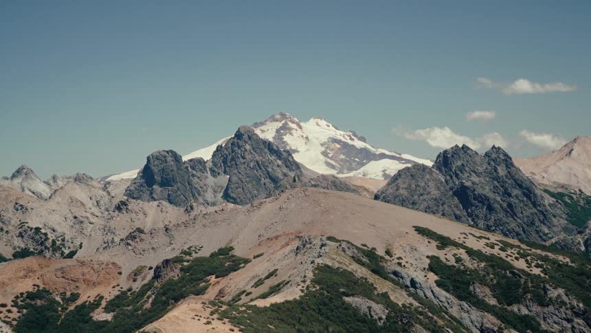 Vegetation covers some mountain slopes while snow covers the highest mountain in a mountain range on a cloudy day