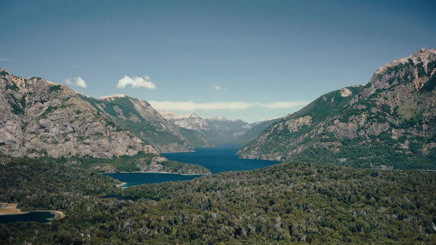 A river flowing beneath a mountain range surrounded by forest in the wild at midday