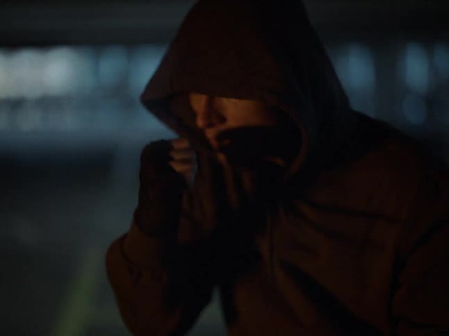 A male boxer wearing a hoodie shadowboxing in an underground parking lot