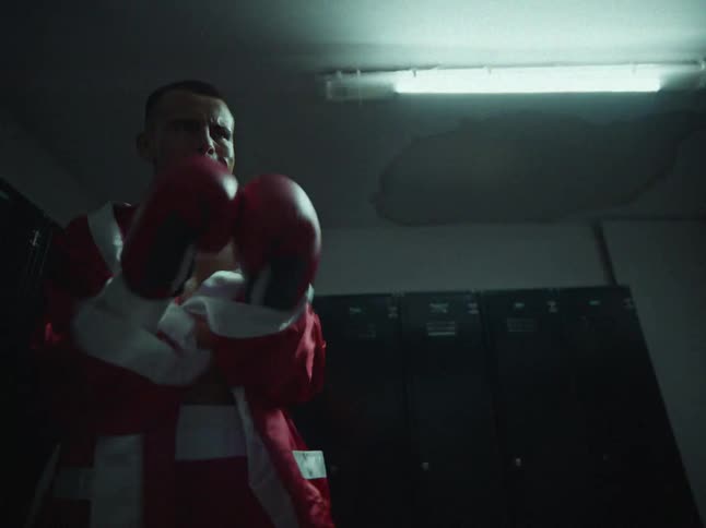 Male boxer standing in the locker room punches the air