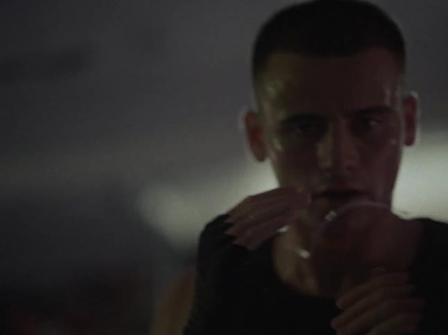 An athletic young man practices boxing in a dimly lit gym