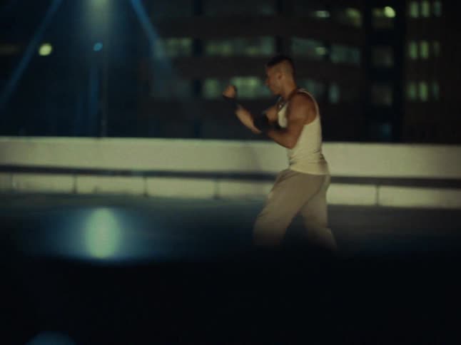 Man shadowboxes while on the roof of an urban building at night