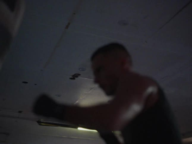 Young adult man training boxing on a punching bag at a gym indoors during day time