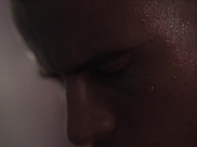 The camera provides an extreme closeup of a persons face highlighting beads of sweat glistening on their skin the scene captures a moment of intense focus and physical exertion with the individual looking downward in a dimly lit environment
