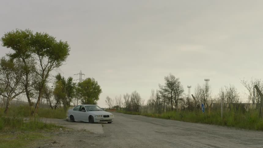 Two people in a car are driving fast and skidding on a rural road