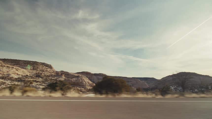 A side view from a moving vehicle captures a desert landscape with mountains and sparse vegetation under a cloudy sky