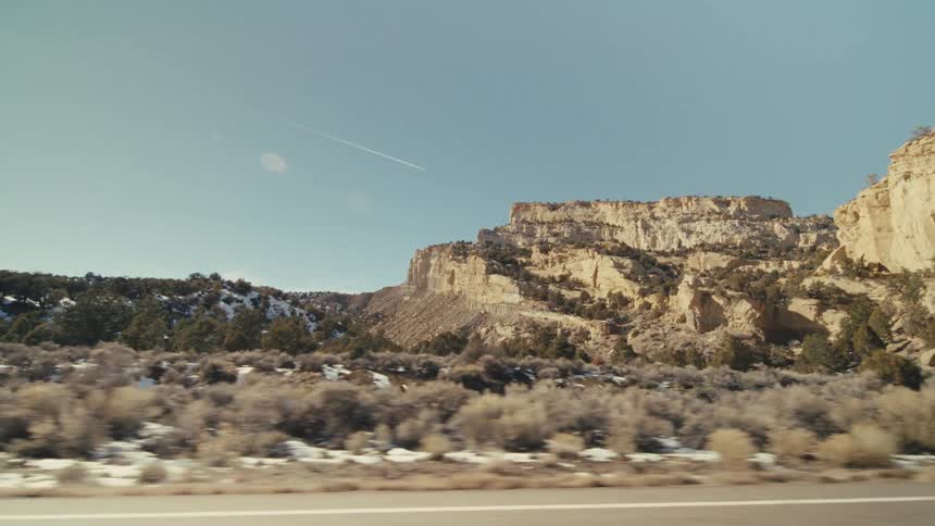 Traveling along a roadway that passes by rocky mountains and plateaus