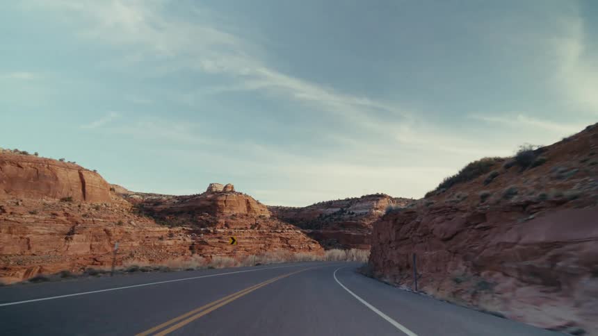 A freeway in the wilderness surrounded by mountains and a canyon at midday