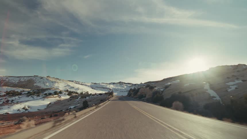 Traveling on a road through mountains with snow on the slopes as the sun shines brightly in the distance