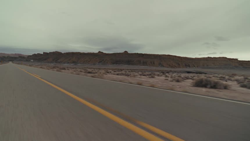 A long highway road passes through a arid landscape with hills