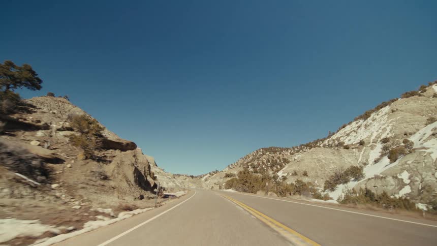 A road trip in the countryside at midday with a mountain range lining the roadside