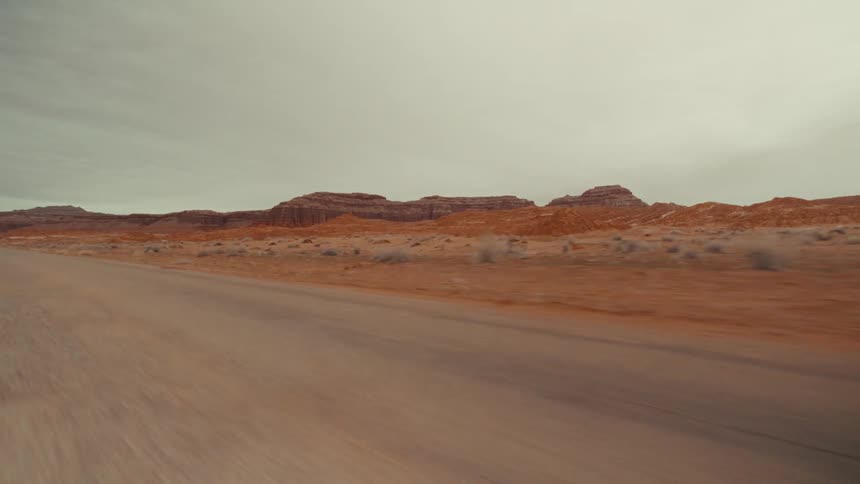 Rural highway passes through arid terrain near the mountains on an overcast day
