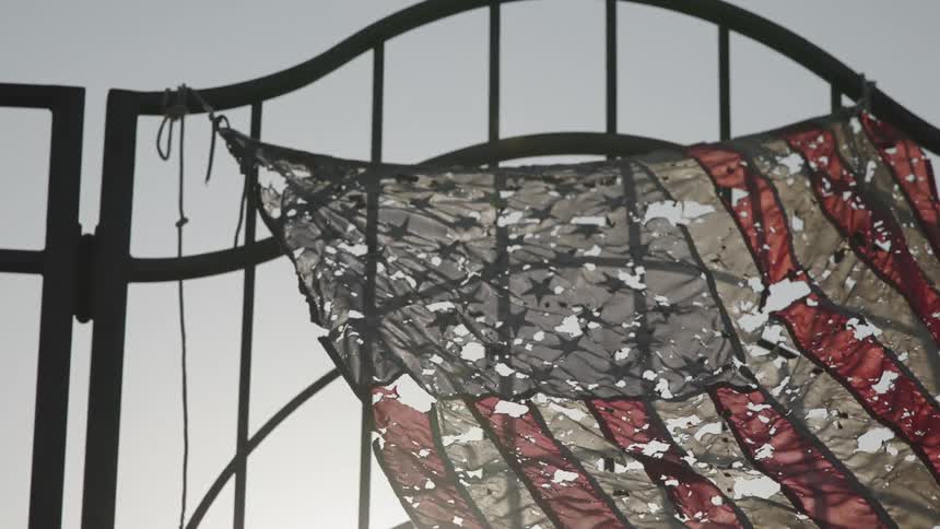 Tattered american flag attached to an iron gate waves in the wind