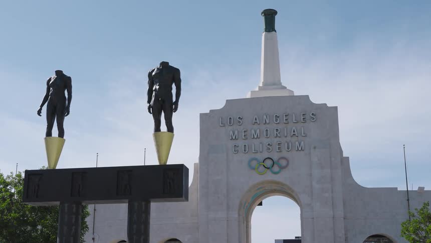 Statues stand in front of the los angeles memorial coliseum on a sunny day