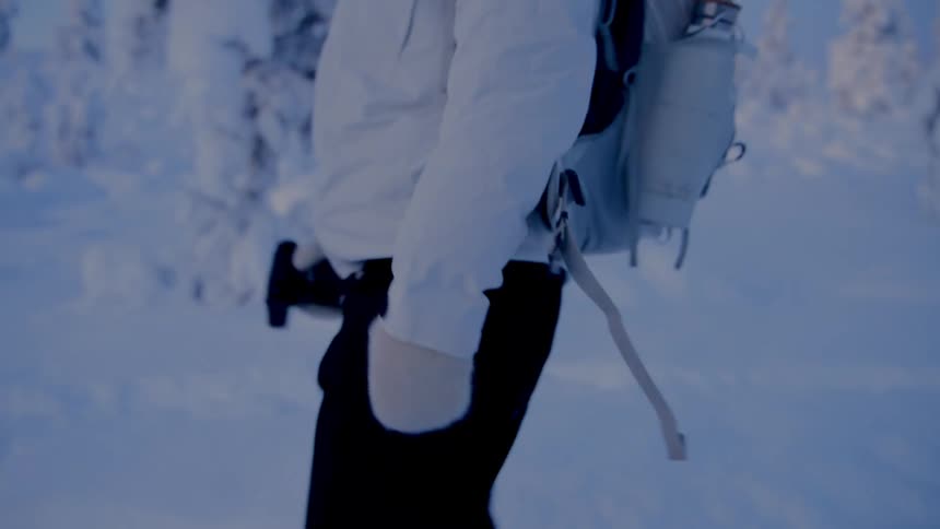 Person wearing a backpack and white jacket walks through a snowcovered environment