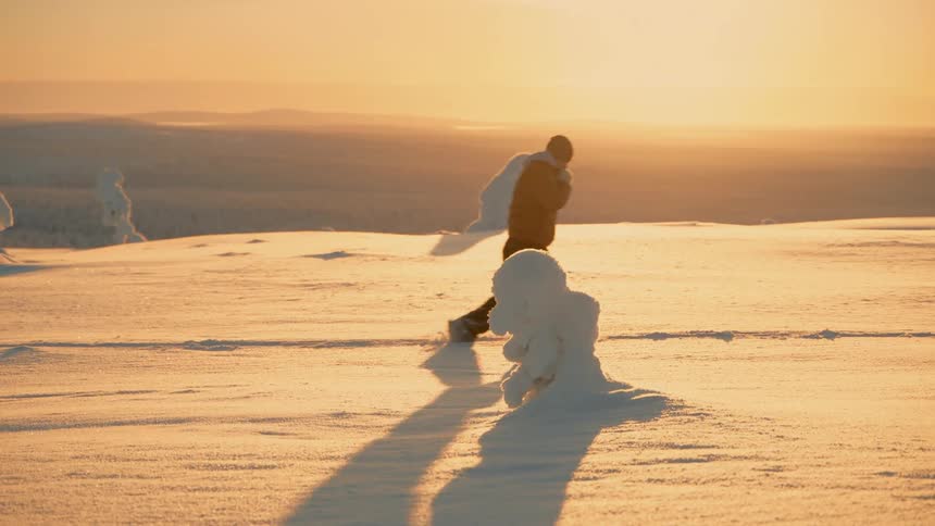 Man walking on a path in the snow on a mountain as the sun shines brightly in the distance