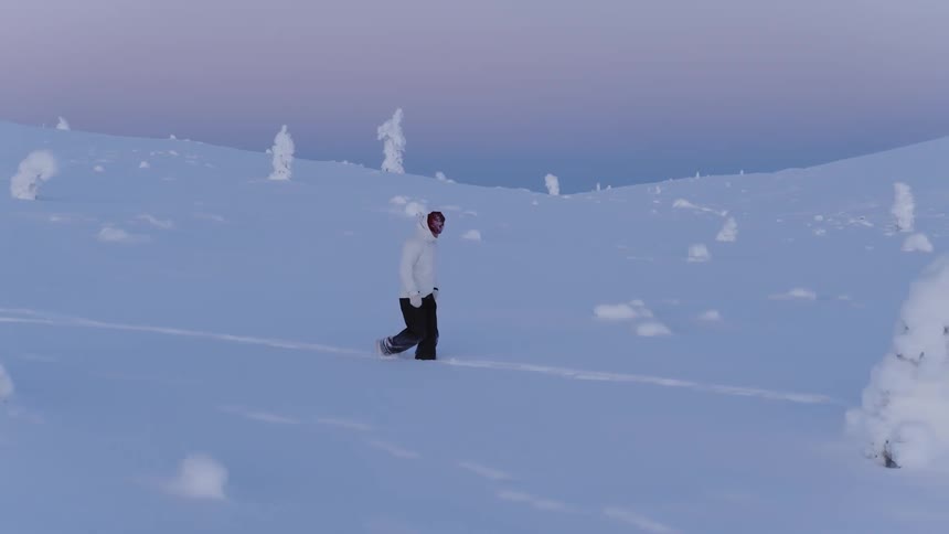 A man is walking through deep snow with treetops sticking out