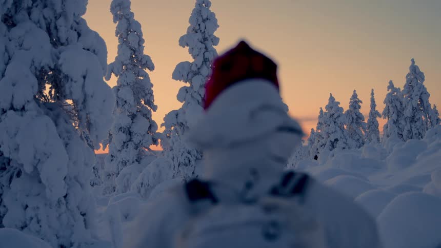 An adult stands in an alpine forest covered in deep snow at sunset