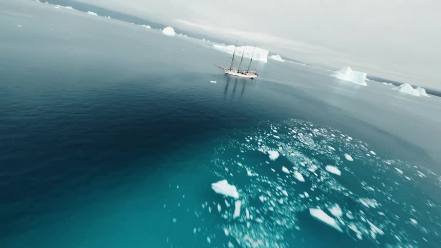 Sailboat floats in the arctic in open water between icebergs