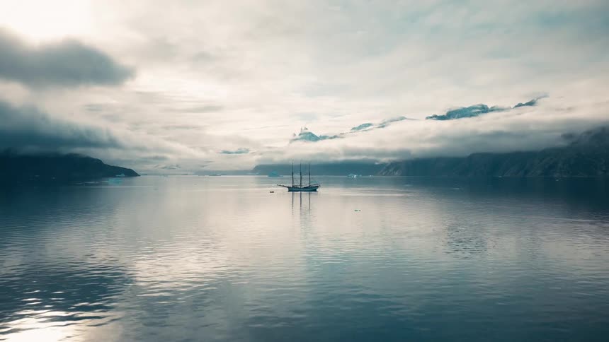 A large sailboat is anchored in calm ocean waters near the coast