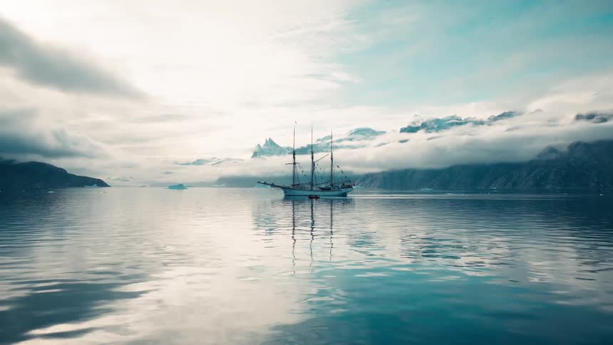 Sailboat anchored on calm waters with mountains and clouds in the background