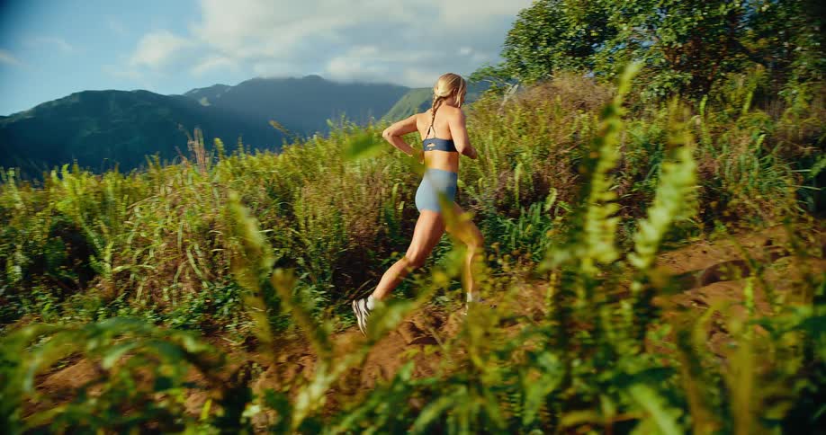 Female runner jogs up along a slight slope as fog covers the mountains in the background on a summer day