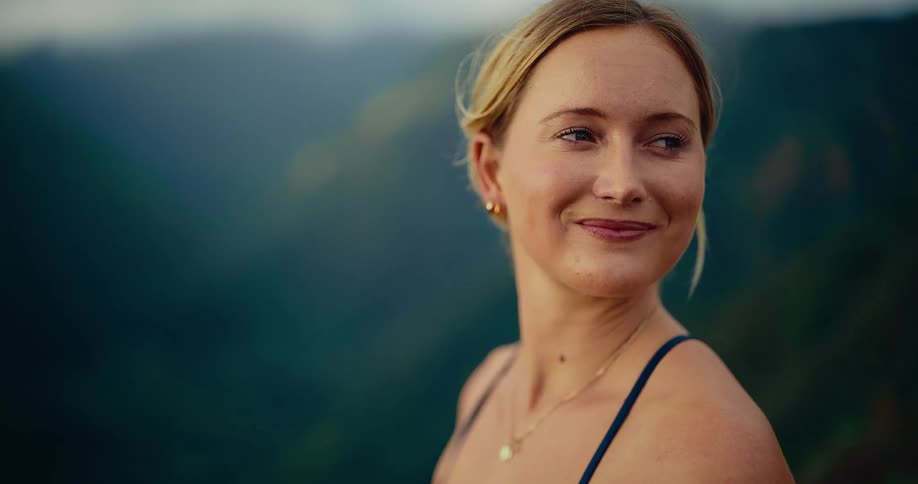 Woman smiles and turns her head as she stands on a mountain