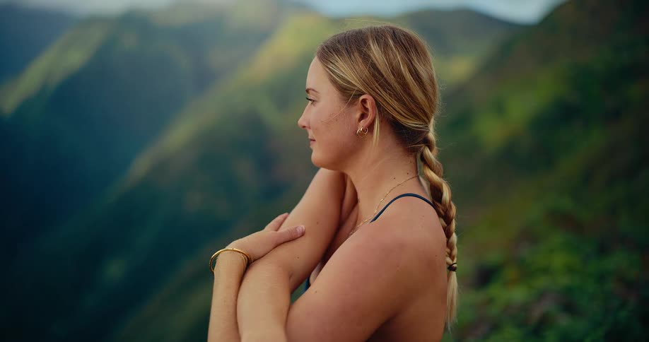 Woman stands at the edge of a mountain as she holds her arms and stretches
