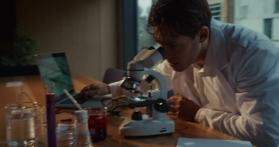 Scientist typing on a laptop computer keyboard and looking into a microscope
