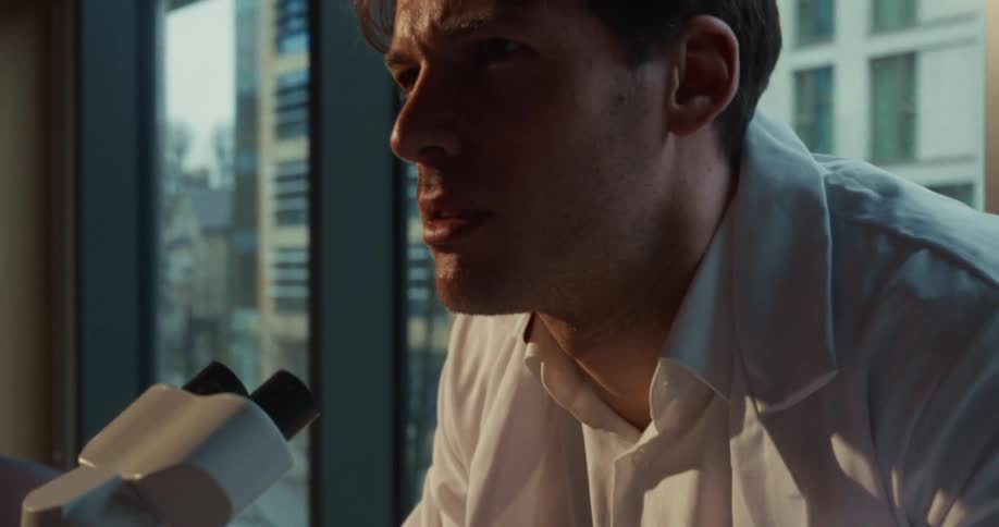 A man looking into a microscope quickly writes down some notes