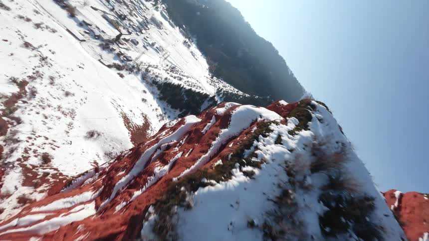 Rugged mountain landscape partially covered in snow the dominant features are large steep rock formations with a striking reddishorange hue characteristic of sandstone