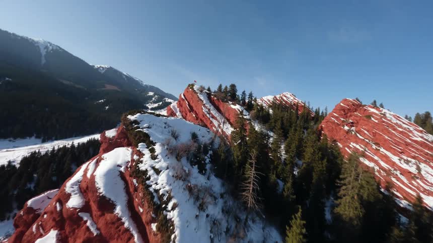 Reddish rock formation with patches of snow and mountains in the background