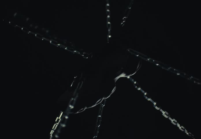 The video features a dark abstract shot of metallic chains extending outward from a central point a persons hands are visible in the middle gripping and manipulating the chains against a black background