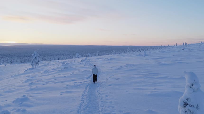 Person walking on a mountain path in the snow with a forest in the valley