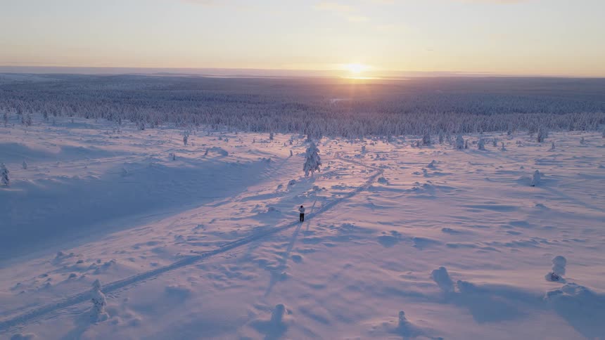 Person walks along a path through the snow as the sun shines from the horizon onto the forest in winter