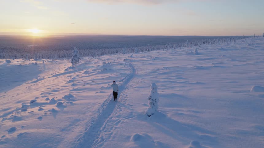 Person walks along a snowy trail at sunset in a vast snowcovered landscape