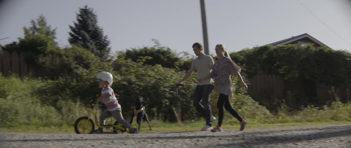 A happy family walks their dog through a quiet suburban neighborhood on sunny day.
