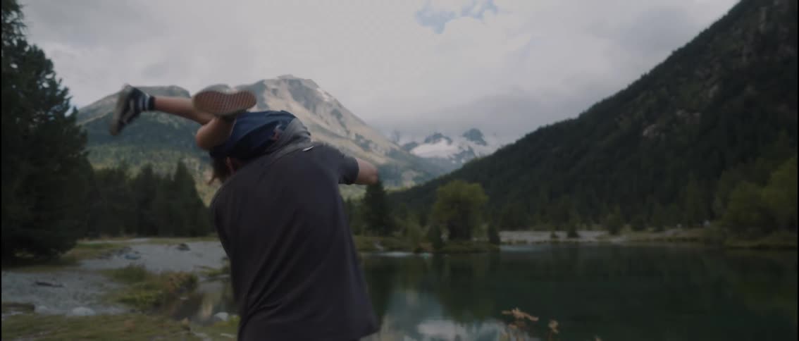 A man playfully swings a young boy around in circles outdoors they are positioned in a scenic mountain landscape next to a calm lake
