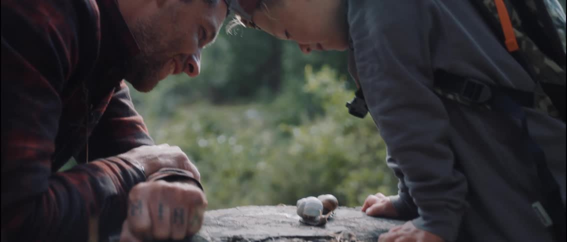 Man and child observe a snail on a log outdoors