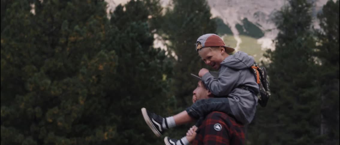 Man walking outside of the forest with his young son on his shoulders covering his mouth with his hand as they play