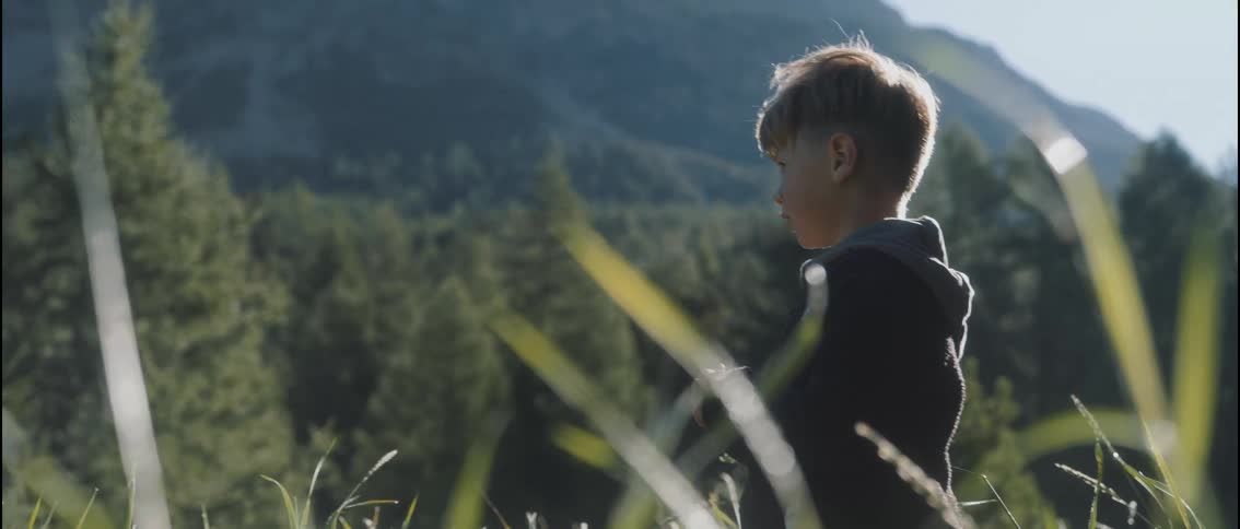 Little boy stands on a mountain overlooking trees in the forested valley
