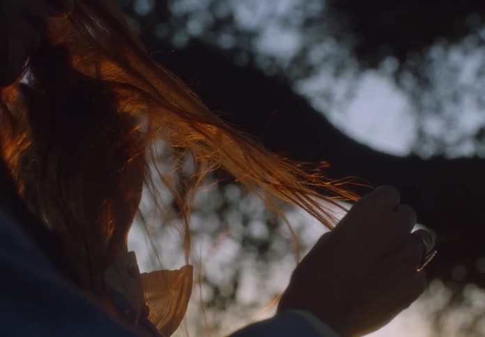Hands hold strands of hair illuminated by sunset light