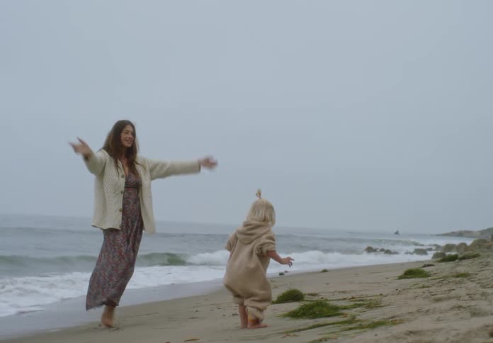 Mother and daughter walk barefoot along the beach by the sea