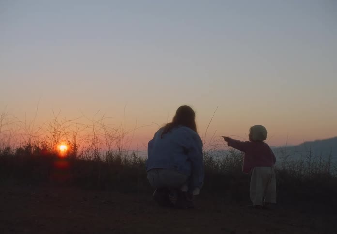 A mother walks with a young girl as the watch the sun set